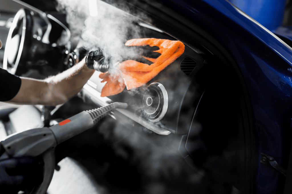 A professional detailer using steam cleaning and a microfiber cloth to deep clean a car's dashboard, an essential step to prepare your car for spring after winter buildup.